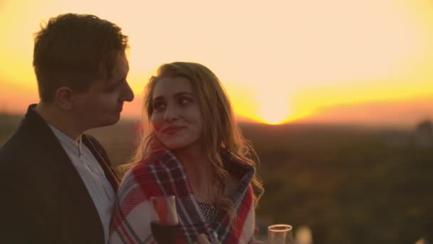 Una joven pareja en el techo bebiendo vino de copas de pie en una manta y admirando la hermosa puesta de sol sobre la ciudad. Noche romántica en la azotea con vistas a la ciudad . — Vídeos de Stock