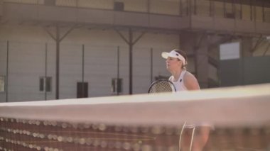 Neşeli atlet tenis topu bekliyor. Usta kadın tenisçi bir topu yenmek için hazırlanıyor. Elinde bir raket tutuyor ve poz yapıyor. Kadın teniste duruyor..