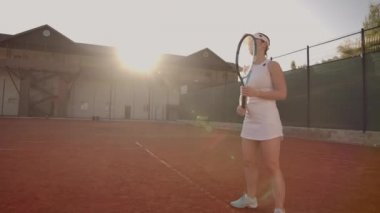 Neşeli atlet tenis topu bekliyor. Usta kadın tenisçi bir topu yenmek için hazırlanıyor. Elinde bir raket tutuyor ve poz yapıyor. Kadın teniste duruyor..