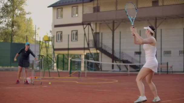Женщина-теннисистка практикуется бить по мячу с тренером, ударяя по мячу ракеткой в замедленной съемке. Обучение теннисистов — стоковое видео