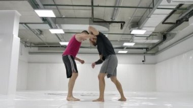 Güreşçi rakibe doğru hareket eder, yavaş çekimde paspasları bitirerek yakalar ve yuvarlar..