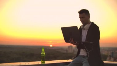 Çatıda dizüstü bilgisayarı olan hippi bir adam. İşyerinde serbest çalışan biri. Kablosuz mobil internet. İnternette çalışıyor.
