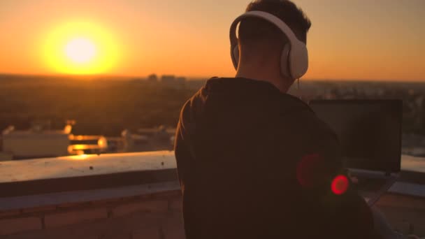 Un homme en casque sur le toit se détend à travailler à distance en profitant de la vie malgré une belle sorte de sipping bière et les types sur le clavier . — Video