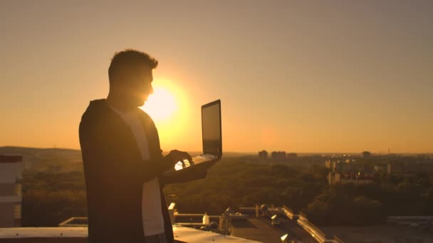 Hacker utilizando el ordenador portátil en la azotea con vista a la ciudad y carta de divisas. Concepto de hackeo y estadísticas — Vídeos de Stock