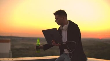 Çatıda dizüstü bilgisayarı olan hippi bir adam. İşyerinde serbest çalışan biri. Kablosuz mobil internet. İnternette çalışıyor.
