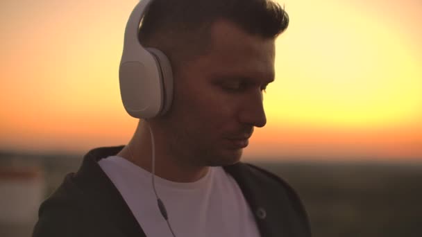 Lächelnd und lachend hört der gut aussehende junge Mann mit drahtlosen Kopfhörern Musik von seinem Smartphone — Stockvideo