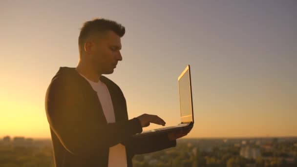 Hacker utilizando el ordenador portátil en la azotea con vista a la ciudad y carta de divisas. Concepto de hackeo y estadísticas — Vídeo de stock