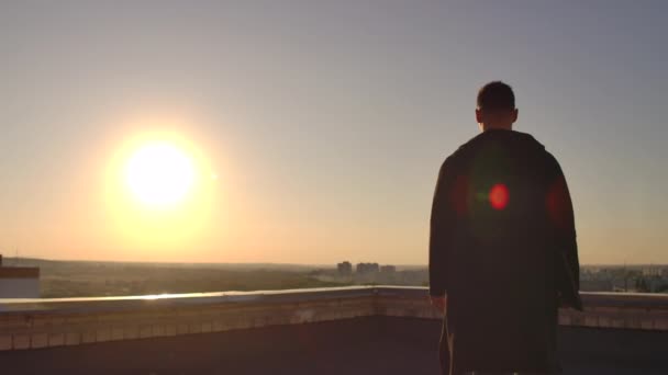 La caméra suit un homme marchant sur un toit au coucher du soleil avec un ordinateur portable et une bouteille. Le pigiste ouvre l'ordinateur portable et tape sur le clavier. Un hacker au ralenti marche sur le toit avec un ordinateur portable — Video