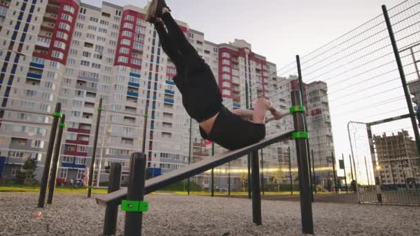 Entrenamiento de hombre fuerte ajuste hacia fuera en barras horizontales al aire libre. Hombre joven entrenando los músculos abdominales levantando las piernas altas a la. Cabeza haciendo flexiones al aire libre durante el — Vídeos de Stock