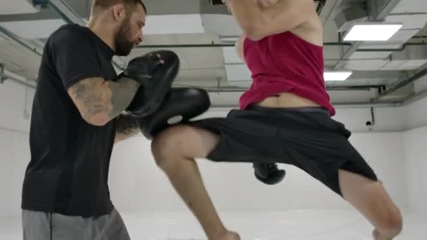 El entrenador y el luchador trabajan la patada en la rodilla de salto en las patas en cámara lenta. Entrenamiento para kickboxing — Vídeo de stock