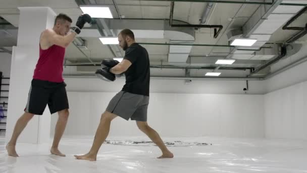 Al entrenamiento en las peleas mixtas el hombre golpea la rodilla a las patas del entrenador en el salto. Movimiento lento — Vídeo de stock