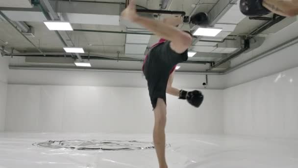 Trage beweging: Fighter slaat toe met een bocht tijdens de rotatie van het been. Coach houdt poten voor kick-bokser training voor de strijd — Stockvideo