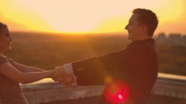 İki aşık bir erkek ve bir kadın gün batımında çatıda gülüp dans ediyorlar. Ağır çekim mutlu çift yazın çatıda