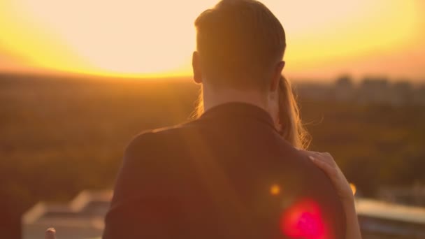 Un hombre y una mujer enamorados bailan parados en el techo de un edificio al atardecer mirándose. — Vídeos de Stock