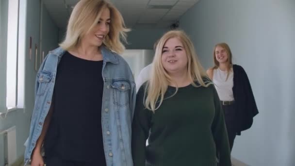 İki kız öğrenci üniversitenin koridorunda yürür ve konuşur, tartışır ve konuşur. — Stok video