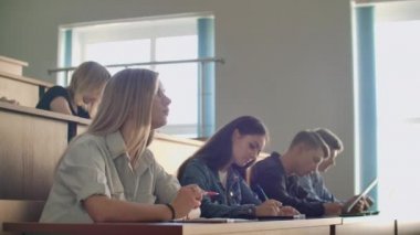 Üniversitenin büyük bir konferans salonunda bir grup erkek ve bayan öğrenci bir profesörün konuşmasını dinliyor.