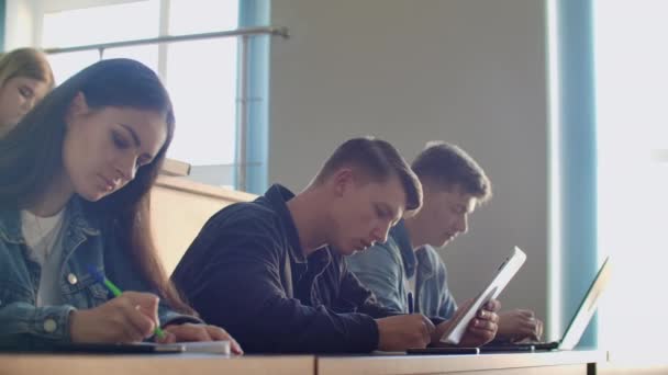 En grupp manliga och kvinnliga studenter i en stor hörsal vid universitetet lyssnar på en föreläsning av en professor — Stockvideo