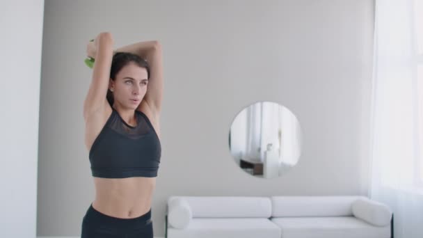 Una joven levanta los brazos con mancuernas detrás de la cabeza haciendo ejercicios de tríceps. Entrenamiento de tríceps — Vídeo de stock