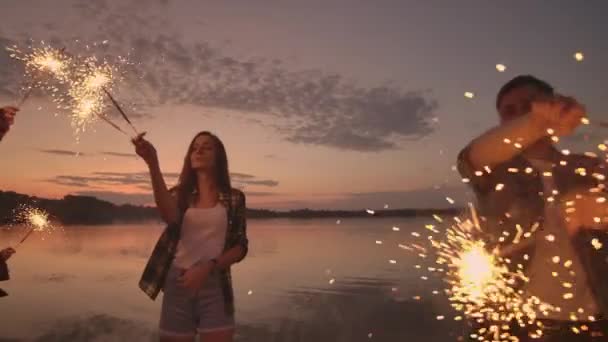 Μια ομάδα φίλων ανδρών και γυναικών γιορτάζουν τις διακοπές στην παραλία με φωτοβολίδες και πυροτεχνήματα. Βραδινό πάρτι αργής κίνησης — Αρχείο Βίντεο