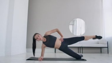 Dairedeki esmer kadın, dizinin üstünde duran ve bacağını kaldıran bir egzersiz tahtası yapıyor. Fitness maratonu