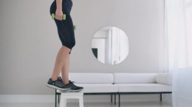 Yakın plan, güzel esmer kadın elinde dambıllarla sandalyeye basıyor.