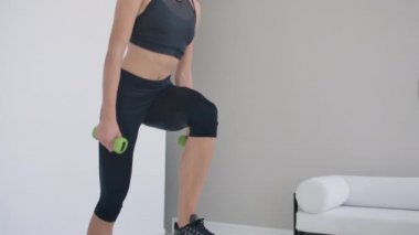 Yakın plan, güzel esmer kadın elinde dambıllarla sandalyeye basıyor.