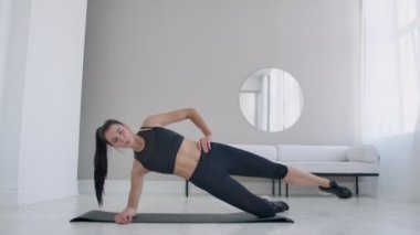 Dairedeki esmer kadın, dizinin üstünde duran ve bacağını kaldıran bir egzersiz tahtası yapıyor. Fitness maratonu
