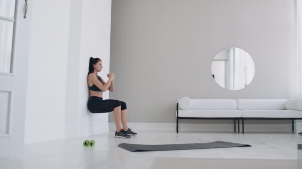En kvinna i statisk ställning utför en ansträngande övning lutande mot en vägg i sittande ställning. Uthållighetsutbildning — Stockvideo