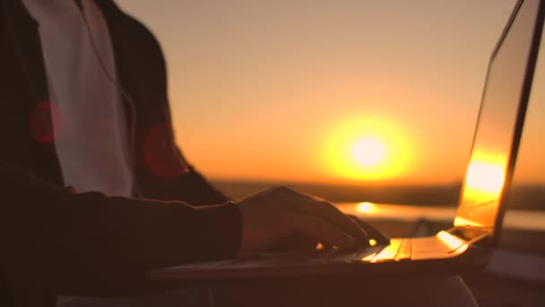 Kluis plan van een hand typen op een laptop toetsenbord bij zonsondergang met uitzicht op de stad van een hoogte. Programmeur werkend op het dak van een gebouw — Stockvideo