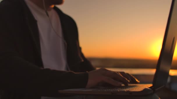 Plano de cofre de uma mão que digita em um teclado de computador portátil no pôr-do-sol com uma visão da cidade de uma altura. Programador trabalhando no telhado de um edifício — Vídeo de Stock