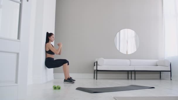 La fille brune gelée dans un squat appuyé sur le mur faisant un exercice statique — Video