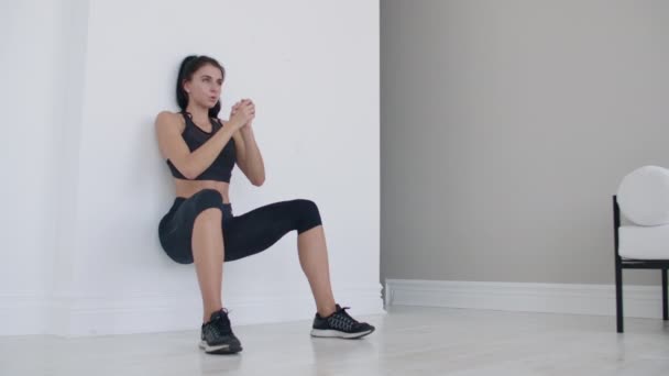 Brunett flickan frös i en huk lutar sig på väggen gör en statisk övning — Stockvideo