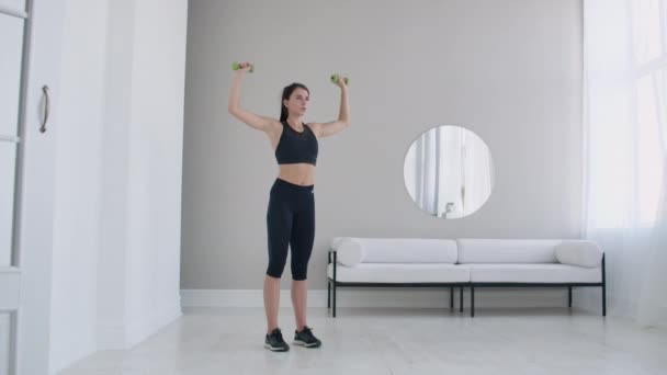 Hijs de halters over uw hoofd uitvoeren van oefeningen voor de schouders. Training thuis in het appartement — Stockvideo