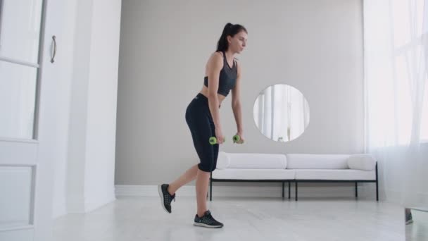 Giovane bella donna bruna in piedi su una gamba facendo curve con i manubri. Esecuzione deadlift con manubri a casa — Video Stock