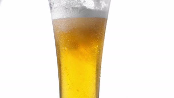 Zeitlupe in Nahaufnahme: Kaltes Bier wird aus einer Flasche auf weißem Hintergrund mit Schaumstoffblasen in ein Glas gegossen — Stockvideo