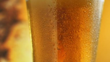 Turuncu sıvıyla dolu bir bardakta kabarcıklar yükseliyor. Su damlalı bir bardakta soğuk light bira. Craft Birası yakın çekim. Döndürme 360 derece