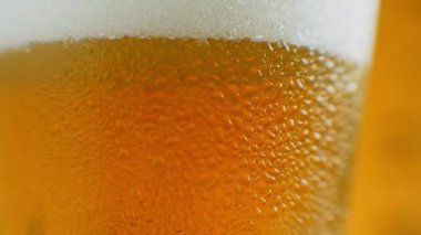 Ağır çekimde yakın çekim: Bardakta soğuk bira büyük damlalar ve bira köpükleri.