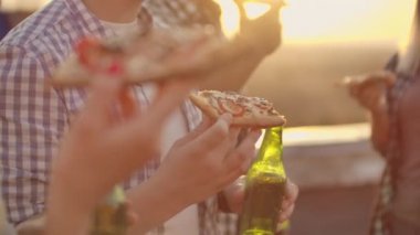 Genç bir adam çatıdaki partide pizza yiyor.