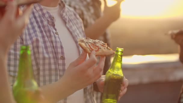 En ung man äter pizza på takfesten. — Stockvideo