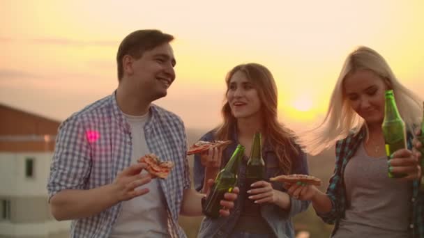 Milující pár pije pivo a jí horkou pizzu na střeše — Stock video