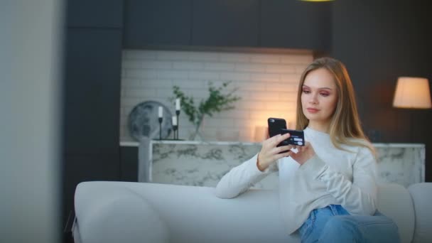En kvinna gör inköp på nätet med hjälp av en smartphone och ett bankkort sitter hemma — Stockvideo