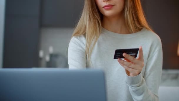 Närbild av en vacker blond kvinna tittar på en bärbar skärm och håller ett bankkort. Nätshopping hemifrån. Betala för frakt, köpa presenter och klänningar till jul. — Stockvideo