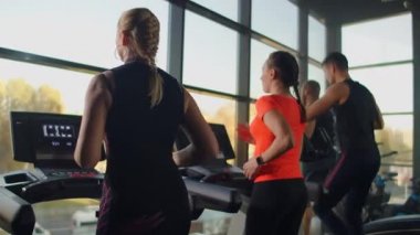 Spor salonunda koşu bandında koşan bir grup insan kardiyo çalışması yapıyor. Erkekler ve kadınlar birlikte antrenman yaparlar. İçeride koşarlar, yavaş çekimde antrenman yapmadan önce ısınırlar.