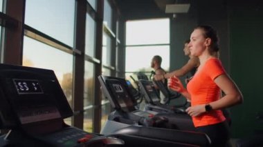 Genç, güzel bir kadın ve spor salonunda koşu bandında koşan üç kişi kardiyo çalışması yapıyor. Yavaş çekimde antrenmandan önce kapalı koşu, ısınma.