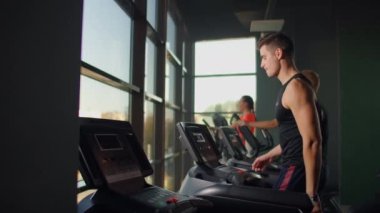 Erkekler spor salonunda koşu bandında yürür. Büyük bir panoramik pencerenin yanında koşu bandında yürüyen bir grup insan. Fitness derslerine başlıyorum. Spor giyim sektöründe genç ve güzel kadınlar ve erkekler.