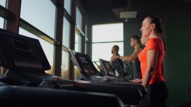 Genç ve güzel bir kız, büyük bir panoramik pencerenin önünde, arka planda yaşayan bir çok insanın önünde ağır çekimde yürüyor.