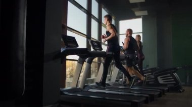 Spor salonundaki büyük bir pencerenin arkasında koşu bandında koşan iki adam. Gençler spor salonunda koşuyor. Spor salonunda aerobik egzersizler.