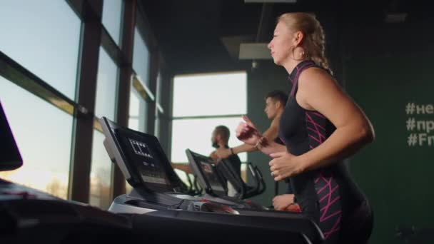Un grupo de personas corriendo en cintas de correr cerca de una gran ventana panorámica. Entrenamiento cardiovascular en grupo . — Vídeos de Stock