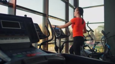 Spor salonundaki sportif formda genç bir kadın eliptik antrenör üzerinde egzersiz yapıyor. Yavaş çekim, eliptik antrenördeki kadın.
