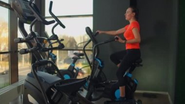 Spor salonunda spor ayakkabılarıyla bisiklet süren genç aktif bir kadın. Hava bisikletinde kadın eğitimi.